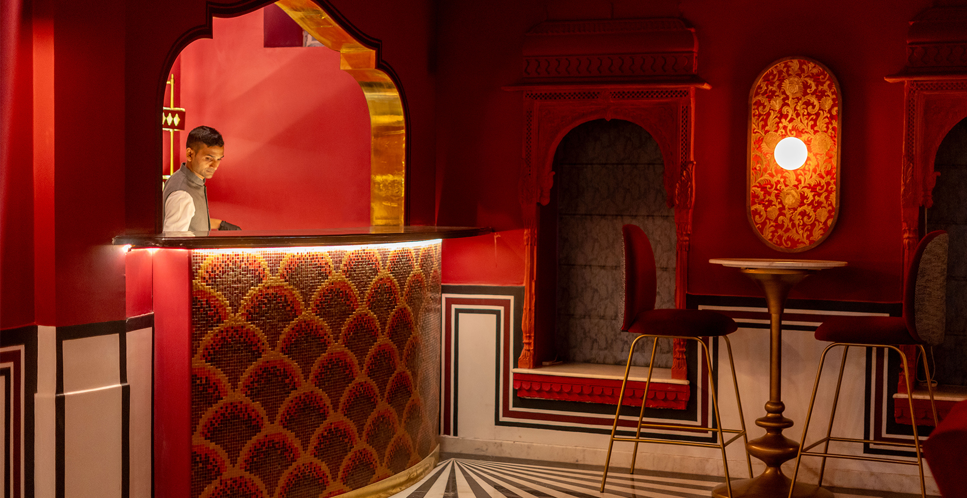 The heritage bar at Padmaa Jaipur — crimson walls, brass fixtures, fish-scale mosaic, black-and-white marble