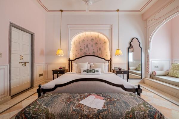 Heritage Suite at Padmaa — pink walls, scalloped arch headboard, Mughal mirror, pendant lamps, block-printed rug